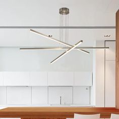 a modern light fixture hanging over a wooden table in a room with white walls and cabinets