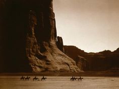 four people are riding horses on the beach in front of large rock formations and cliffs