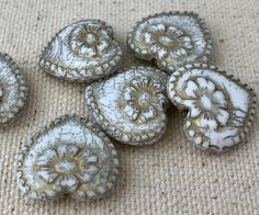 five pieces of white and gold glass with designs on them sitting on a beige surface