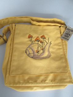 Embroidered 100% cotton canvas messenger bag with snail & mushroom design the bag colour is <ustard yellow the bag measures height 29cm's, width 26cm's, depth 10cm's it has an adjustable strap, two generous front pockets and a zip front pocket, the main part has a zip closure and a zip pocket to the back. the embroidered design colours can be customised please message me with your requirements. Snail Mushroom, Aran Weight Yarn, Mushroom Design, Canvas Messenger Bag, Crochet Applique, Embroidered Bag, Timeless Treasures, Cute Bags, Embroidered Design