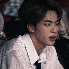 a young man wearing a white shirt and black tie sitting in front of a crowd