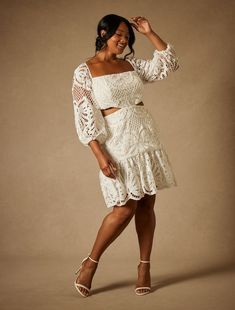 a woman in a white dress posing for the camera with her hand on her head