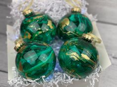 three green glass ornaments sitting on top of a white box with gold trimmings