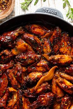 a skillet filled with chicken wings and garnished with seasoning on top