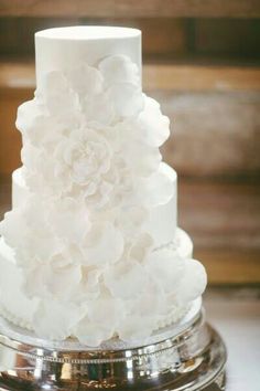 a three tiered white wedding cake with flowers on the top and bottom, sitting on a silver platter