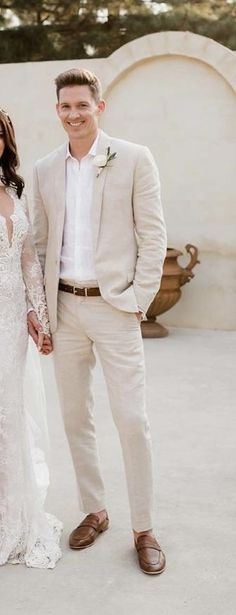 a bride and groom standing next to each other in front of a white stucco wall