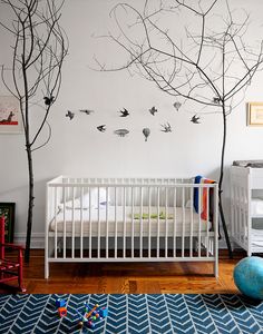 a baby's room with white crib and trees on the wall