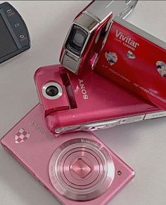 a pink camera sitting on top of a table next to a cell phone