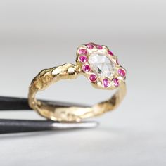 a gold ring with pink and white stones on it next to two black tongs