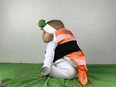 a baby sitting on top of a green sheet wearing a white and orange striped blanket