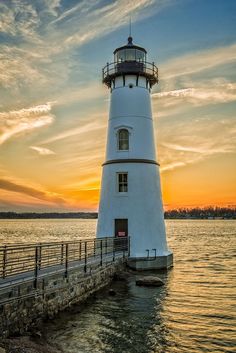 a light house sitting on top of a pier next to the ocean at sunset or dawn