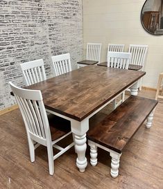 a dining room table with white chairs and wooden benches on the floor next to a brick wall