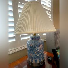 a lamp sitting on top of a wooden table next to a window covered in blinds