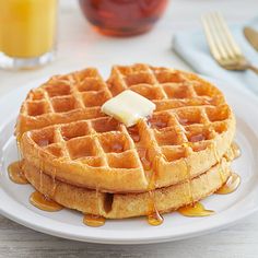 a white plate topped with waffles covered in syrup next to a glass of orange juice