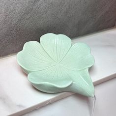 a green flower shaped bowl sitting on top of a white counter next to a faucet