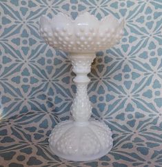 a white vase sitting on top of a table next to a blue and white wall