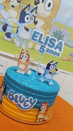 a blue cake with cartoon characters on it sitting on top of an orange tablecloth