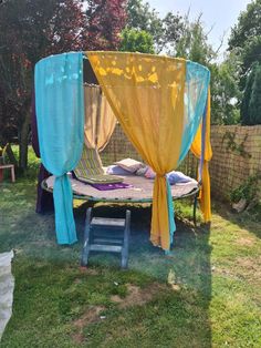 a canopy bed in the middle of a yard with blue and yellow drapes on it