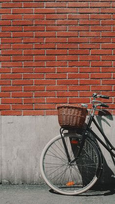 a bicycle leaning against a brick wall with a basket on the front wheel and handlebars