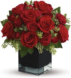 red roses in a black square vase with greenery on the bottom and green leaves