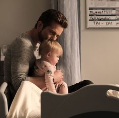 a man holding a baby in his arms while sitting on a hospital bed next to a window