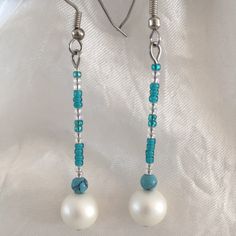 a pair of white pearls and turquoise beads are hanging from silver earwires on a white background