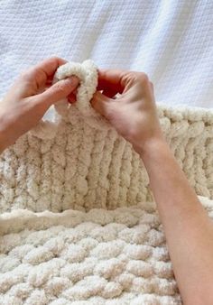 two hands are crocheting the ends of a white blanket on top of a bed