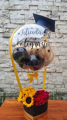 a graduation hat with balloons and flowers on a table in front of a brick wall