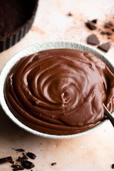 a bowl filled with chocolate frosting on top of a counter next to a cupcake