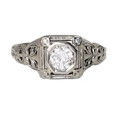 "This is an exemplary 18K white gold Art Deco engagement ring! It features a 30-point Euro Cut diamond of very high quality, in a hexagon setting. This extraordinary ring has a square face with decorative corners, and the head has lacy openwork. The sides of the ring also have ornate embossed and cut-out designs that taper down to a simple shank. An elegant choice for your lady! Vintage: 1930s Size: 5 3/4 Materials: 18K White Gold, Diamond Marked: 18KT. Diamond: 4.4mm, 30 point Old Euro Cut, VS- Formal White Ring With Single Diamond, Art Deco Octagon Diamond Ring In Diamond White, Classic Octagon Ring With Diamond Accents, Silver Art Deco Diamond Ring With Octagon Shape, Art Deco Diamond White Octagon Diamond Ring, Silver Octagon Diamond Ring For Wedding, Elegant Octagon Diamond Promise Ring, Art Deco Octagon Diamond White Ring, Silver Octagon Art Deco Diamond Ring