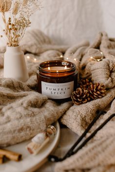 a candle sitting on top of a white plate next to a pile of blankets and candles