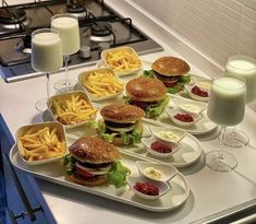 several trays filled with sandwiches and french fries on a counter next to glasses of milk