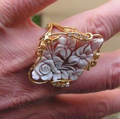 a woman's hand holding a ring with flowers on it and gold chains around the band