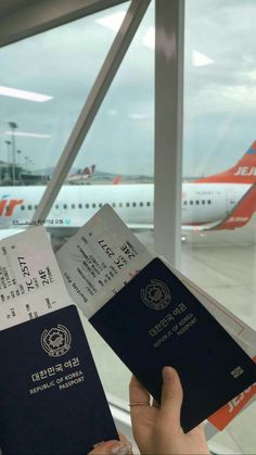 two people holding up their passports in front of an airport window