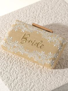 Meet your favorite summer clutch for the bride to be in your life, the Fiorentina "Bride" Minaudiere from Shiraleah. This clutch features a floral embroidery and the text "Bride" in gold cursive lettering and a wooden closure. This bag will go perfectly with any of the bride to be's outfits making it look chic and sophisticated. Measuring L 8" × W 2" × H 4.25"; and a 23" L cross body chain , the Fiorentina "Bride" Minaudiere effortlessly exudes style and sets a statement. Pair with other items f Gold Evening Bag For Summer Wedding, Elegant Summer Wedding Clutch, Summer Wedding Clutch Evening Bag, Gold Clutch For Formal Summer Events, Gold Embroidered Clutch For Wedding, Embroidered Clutch As Summer Gift, Embroidered Clutch For Summer Gift, Embroidered Clutch Gift For Summer, Elegant Embroidered Clutch For Summer