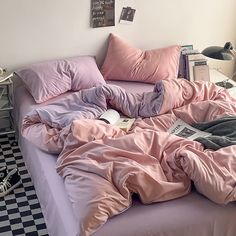 an unmade bed with pink sheets and pillows on it, in a room with black and white checkered flooring