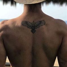 a man with a hat on his head looking out at the ocean while wearing a bird tattoo