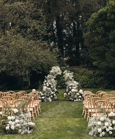 rows of chairs with white flowers on them in the grass next to some trees and bushes