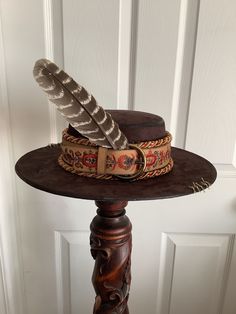 This is a custom weathered hat with incredible detail.  Brown suede hat wIth decorative leather trim and brass bucke.  Topped with feathers, multi colored cording, vintage buttons and tan stitching.  Adjustable band in side. Brown Hat Bands With Feathers For Western-themed Events, Rustic Brown Top Hat With Flat Brim, Vintage Brown Fedora With High Crown, Vintage High Crown Brown Fedora, Rustic Brown Brimmed Top Hat, Vintage Fedora Mini Hat For Festivals, Rustic Brown Top Hat For Western-themed Events, Rustic Adjustable Brown Top Hat, Country Style Brown Hat With Feathers