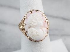 "Cameo is the art of carving a layered material, creating a portrait or landscape in different colors and textures. Shell is the traditional medium for this artwork. This superb cameo ring is unusual; the shell is a soft baby pink color, with the lady and background being the same color, and comes carved from a Caribbean conch shell, as opposed to the more often seen Mediterranean conch shell. Set into a lovely gold filigree mounting dating from the 1970s, this is truly a sweet vintage piece! Me Vintage Cameo Jewelry, Yellow Gold Sapphire Ring, Baby Pink Color, Baby Pink Colour, Cameo Jewelry, Cameo Ring, Vintage Cameo, Conch Shell, Gold Filigree