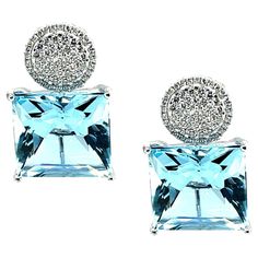 These bold earrings feature two spectacular square-cut aquamarines that weigh a total of 26 carats. The aquamarines have a deep blue color and are very large, measuring 15mm across. It is highly unusual to find a beautifully matched pair of aquamarines of this large size. They are brilliant-cut, similar to princess-cut diamonds, which gives them additional brilliance and life! Over a hundred white diamonds are pave-set in 18k white gold solid circles with outer frames that sit above the aquamari