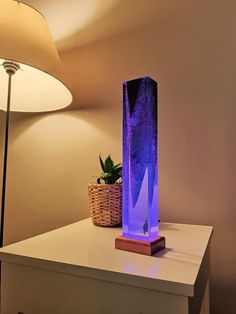 a purple lamp sitting on top of a white table next to a basket with plants