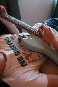 a person laying down with a guitar in their lap and one hand on the neck