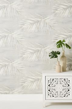 a white cabinet with two vases and a plant in front of a wallpapered background