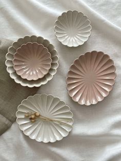 three pink plates sitting on top of a white bed next to a gray and white pillow