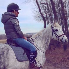 a woman riding on the back of a white horse in a wooded area with trees