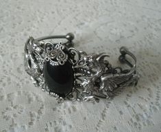 This beautiful silver plated filigree cuff bracelet has silver plated dragons, silver plated accents and a black onyx setting. Adjustable. Elegant Adjustable Dragon Design Jewelry, Elegant Adjustable Jewelry With Dragon Design, Gothic Metal Jewelry With Dragon Design, Black Jewelry With Dragon Design Collectible, Collectible Black Jewelry With Dragon Design, Silver Fantasy Jewelry With Dragon Design, Fantasy Silver Jewelry With Dragon Design, Silver Fantasy Engraved Jewelry, Silver Engraved Fantasy Jewelry