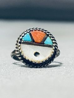 "MAKE US AN OFFER BY CLICKING THE \"MESSAGE SELLER\" Button- This is a striking vintage Zuni inlaid sun face silver ring. This wonderful ring contains a detailed inlaid sun face that includes mother of pearl, turquoise and coral. Bordering the entire round sun face is a silver rope. This ring contains old natural patina and is just so beautiful. The ring face measures around 5/8\" x 5/8\". The ring size is around 5. Cir. Mid century . Sterling silver. Sturdy 2 grams. Make Us an Offer- Due to the Artisan Turquoise Ring Round Collectible, Artisan Round Turquoise Ring Collectible, Artisan Round Turquoise Collectible Ring, Southwestern Multicolor Turquoise Ring, Adjustable Vintage Jewelry With Sun Design, Vintage Multicolor Multi-stone Turquoise Ring, Vintage Multicolor Inlay Jewelry, Vintage Multicolor Inlaid Jewelry, Adjustable Multicolor Turquoise Ring