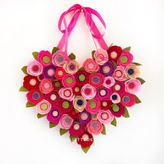 a heart shaped origami flower arrangement hanging on a wall with a pink ribbon