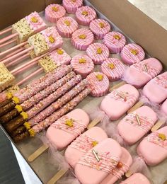 a box filled with lots of pink and yellow decorated cookies next to other treats on sticks